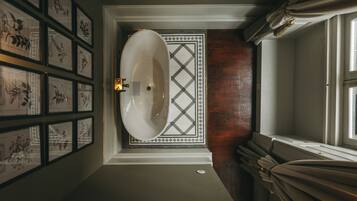 A bathroom with a large oval sink, framed artwork on the walls, a tiled floor, and a window with curtains.