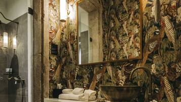 Une salle de bain dotée d’un grand miroir, de décorations murales raffinées, d’un lavabo avec un receveur de style ancien et d’un porte-serviettes.