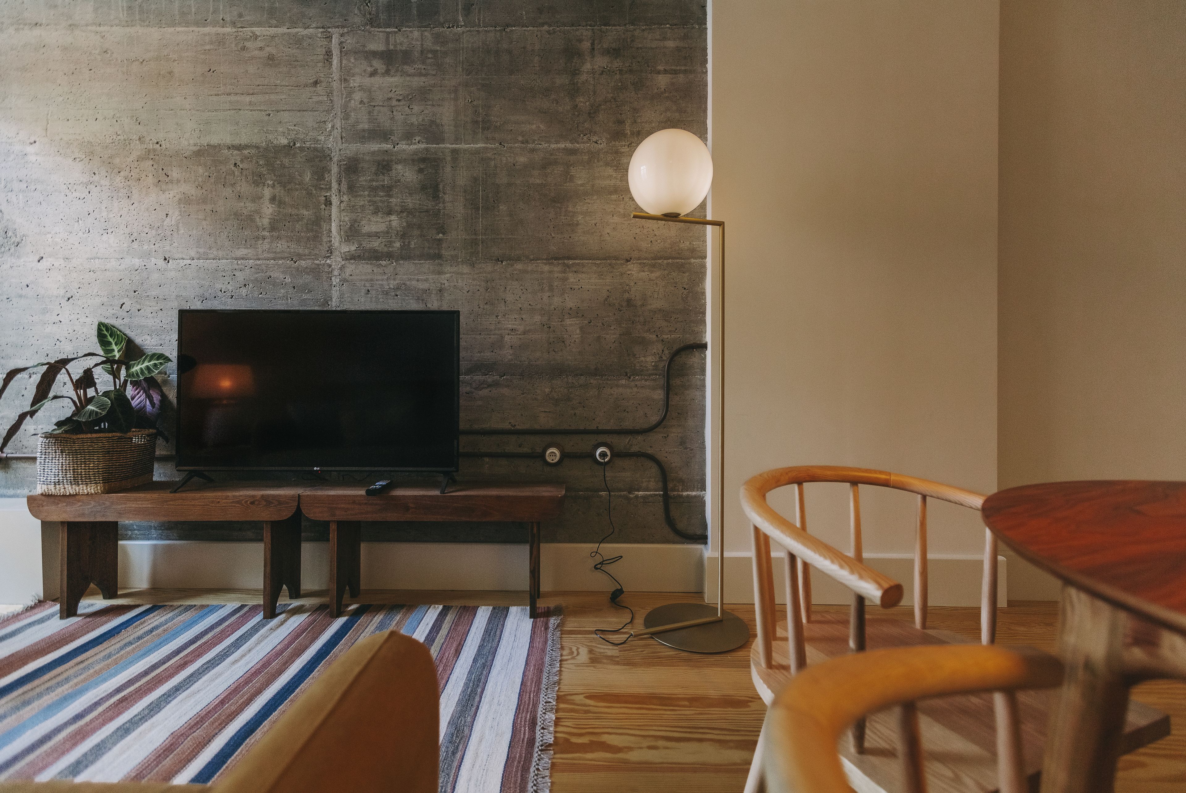 A living room with a television on a wooden stand, a lamp, a dining table, and a striped rug.