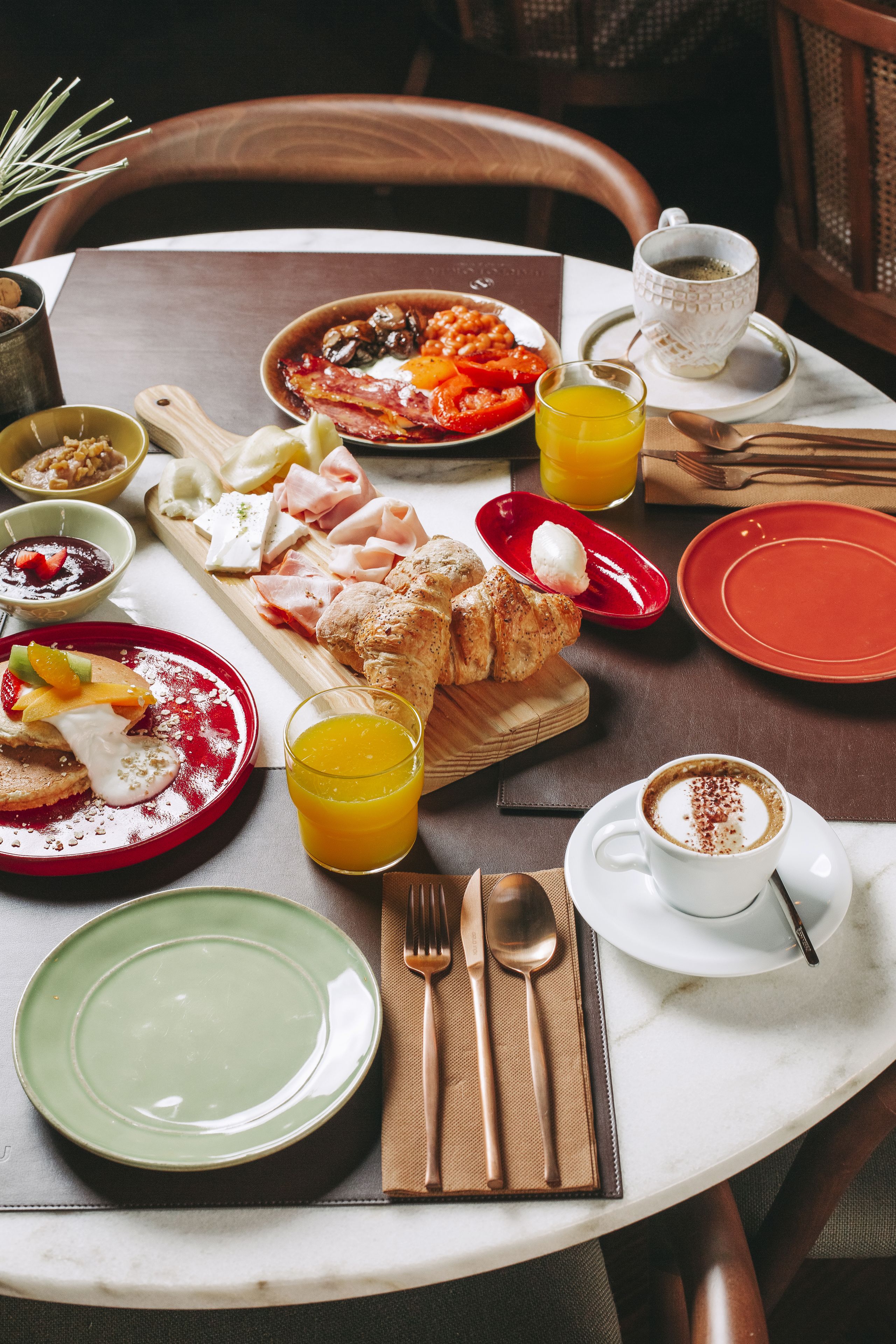 Ett frukostbord med olika rätter, inklusive ägg, rostat bröd och bakverk, samt en kopp kaffe och ett glas apelsinjuice.