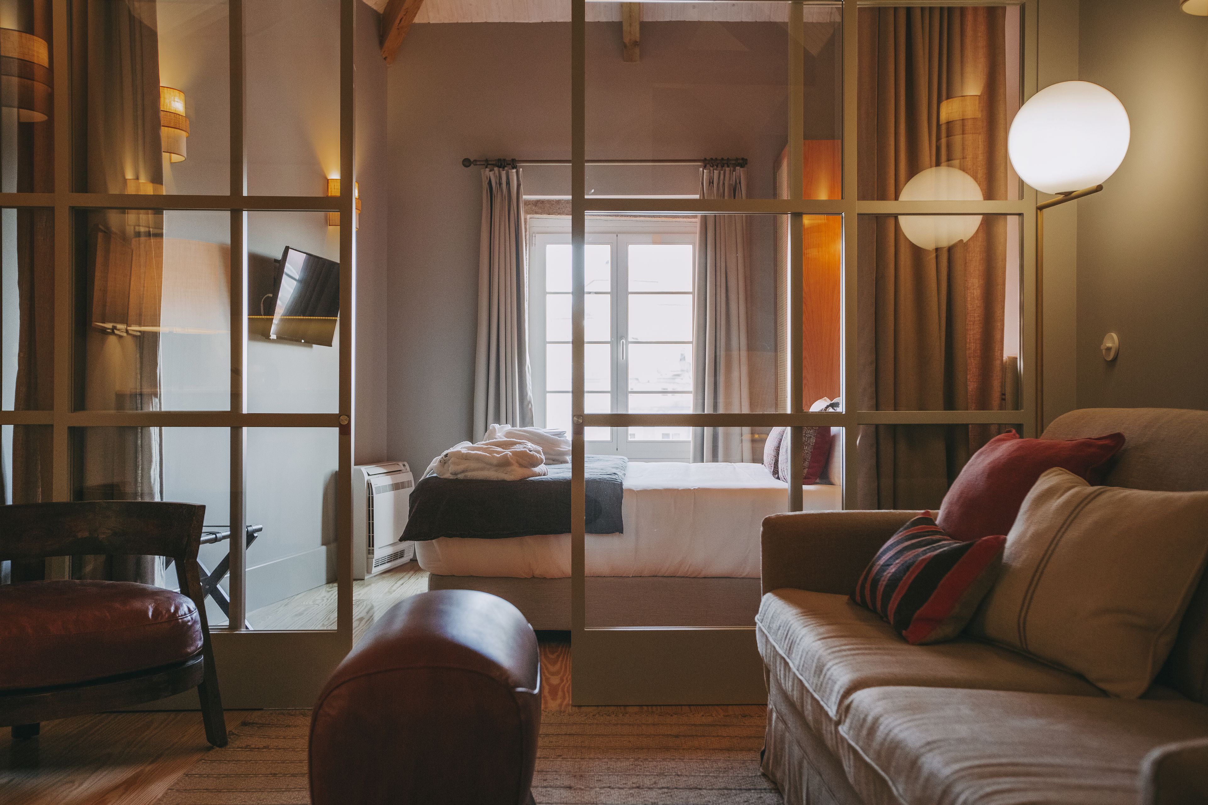 A modern hotel room with a large mirror, a sofa, a bed, and a television.