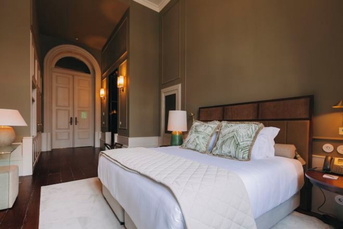 A hotel room with a large bed, a nightstand, a lamp, a desk, and a chair.