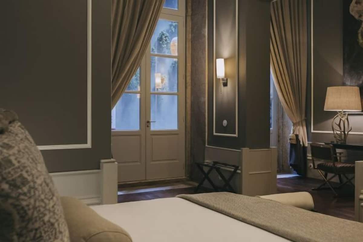 Hotellihuone, jossa on sänky, verhot, työpöytä, tuoli ja lamppu.