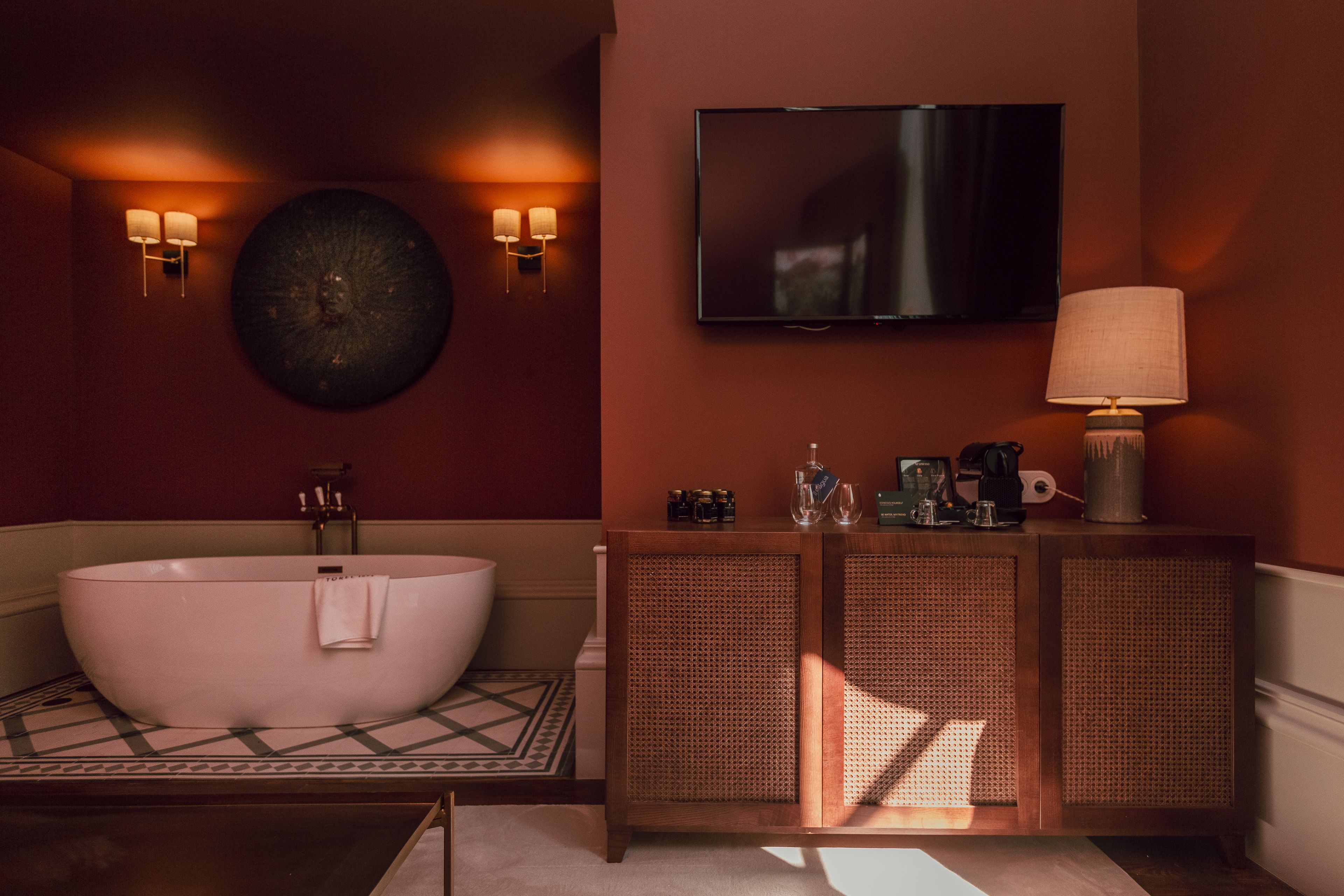 A modern bathroom with a freestanding bathtub, a flat-screen TV mounted above the sink, and a cabinet with toiletries.