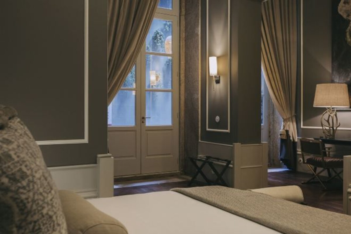 A hotel room with a bed, curtains, a desk, a chair, and a lamp.