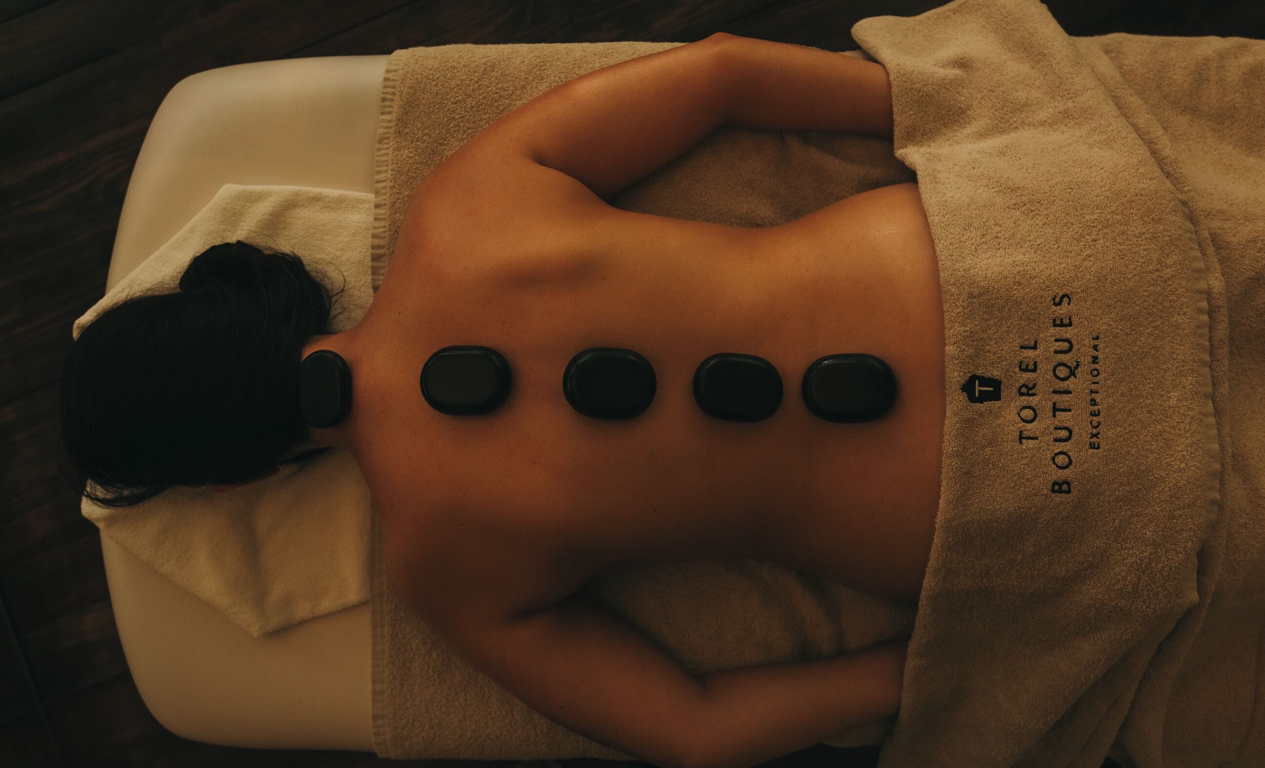 A person receiving a massage with four black stones placed on their back.