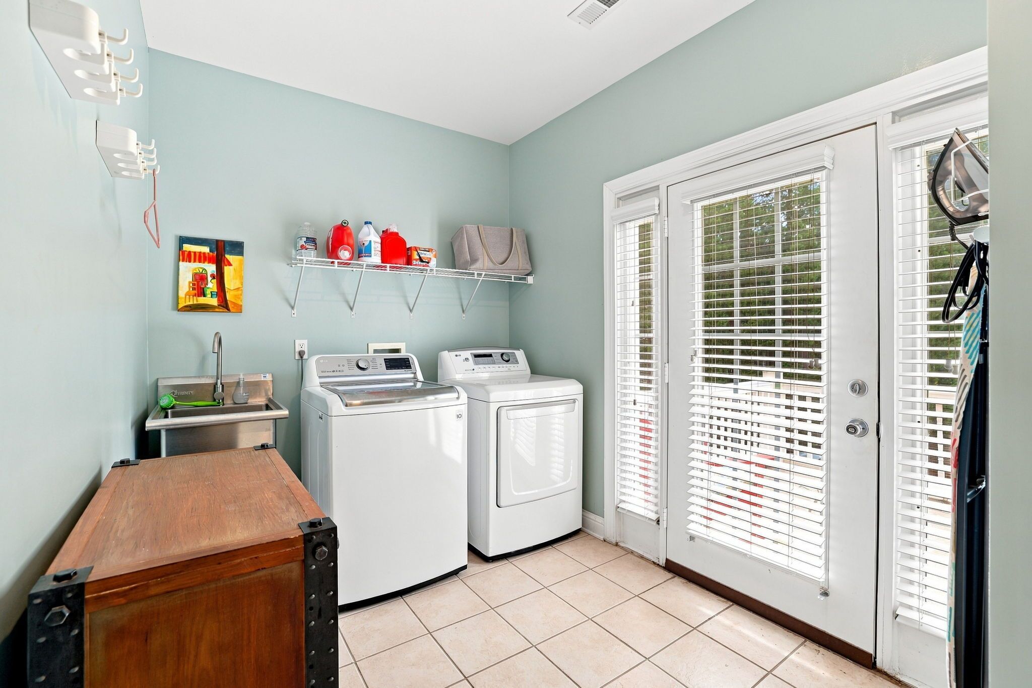 A laundry room with two washing machines, a drying rack, and a shelf with cleaning supplies.