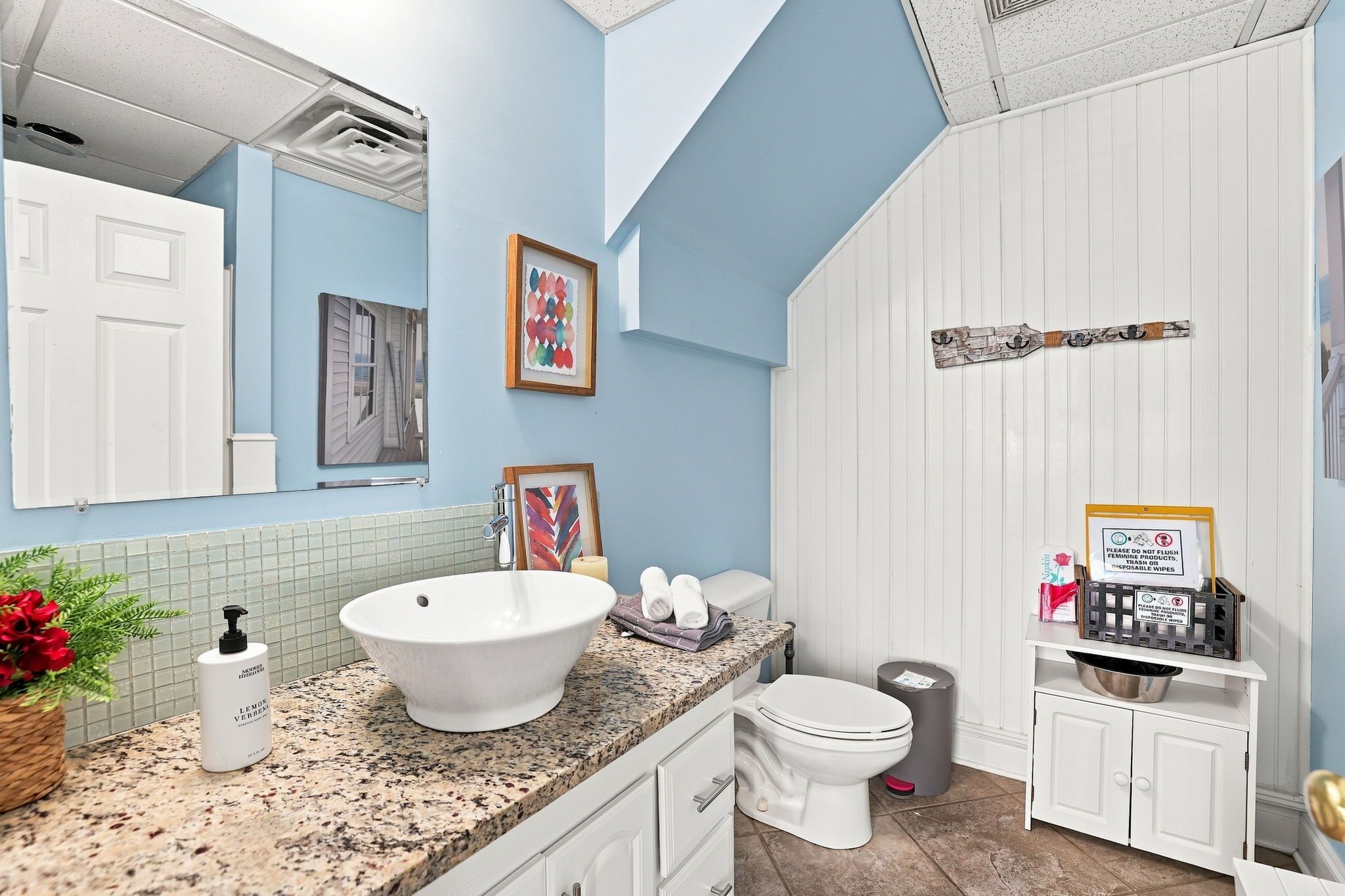 A bathroom with a large white sink, a toilet, a trash can, and a shower area.