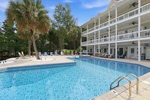 A pool with lounge chairs and a multi-story building with balconies. - Luxury Lake House, Pool, Hot tub, Dock, Beach, Game room, Boat Rental available (Charlotte)