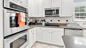 A modern kitchen with stainless steel appliances, white cabinetry, and a tiled backsplash. - Luxury Lake House, Pool, Hot tub, Dock, Beach, Game room, Boat Rental available (Charlotte)
