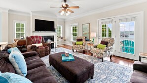 A spacious living room with a fireplace, a large flat-screen TV, and a view of the outdoors through a sliding glass door. - Luxury Lake House, Pool, Hot tub, Dock, Beach, Game room, Boat Rental available (Charlotte)
