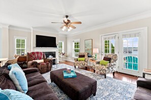 A spacious living room with a fireplace, a large flat-screen TV, and a view of the outdoors through a sliding glass door. - Luxury Lake House, Pool, Hot tub, Dock, Beach, Game room, Boat Rental available (Charlotte)