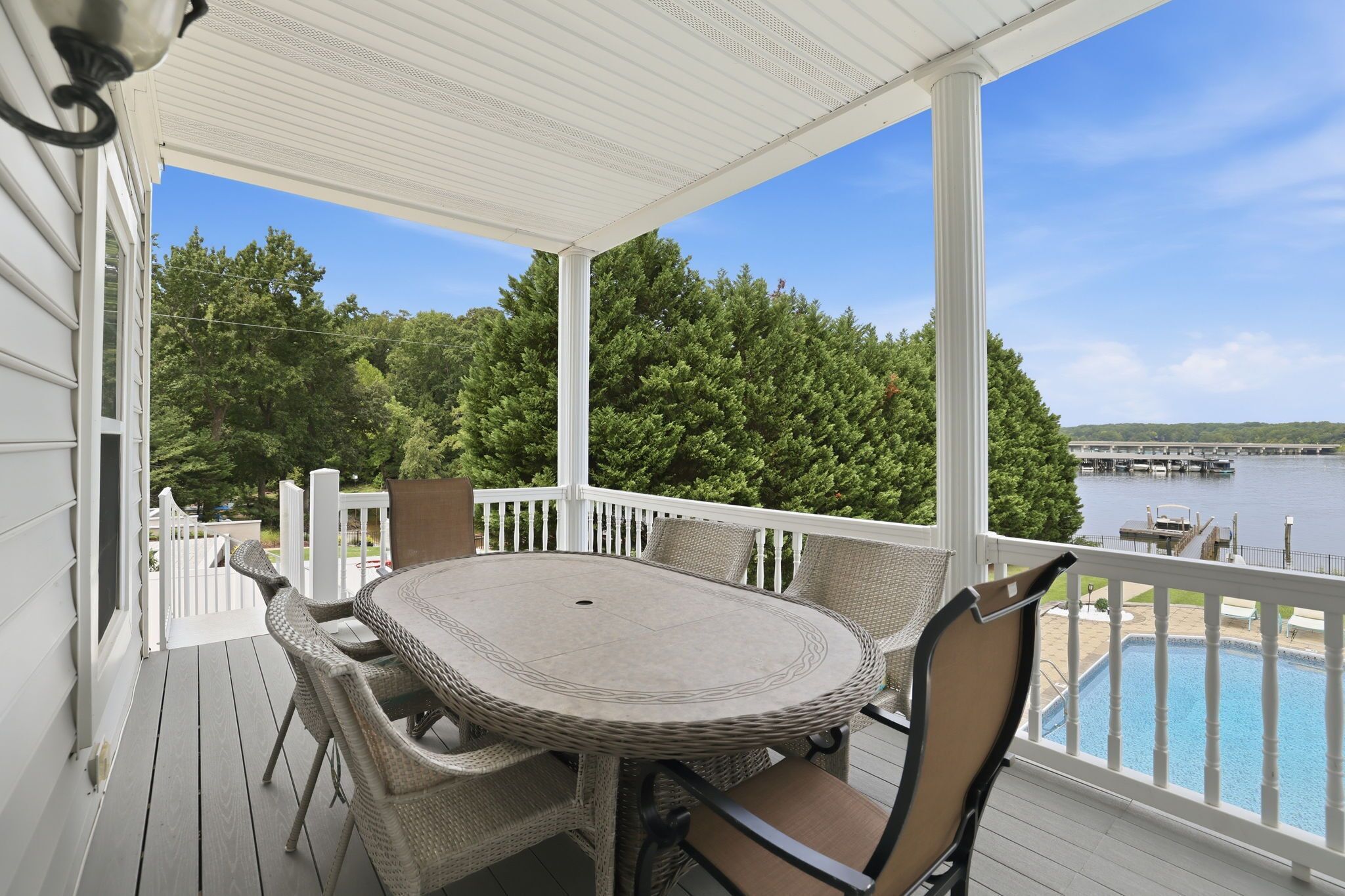 A covered outdoor area with a round table and chairs, a view of a lake, and a dock with boats.