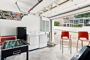 A garage with a washing machine, a foosball table, and two red chairs. - Luxury Lake House, Pool, Hot tub, Dock, Beach, Game room, Boat Rental available (Charlotte)