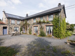 A stone house with a gravel driveway, a patio with a table and chairs, and a garden with various plants and flowers.