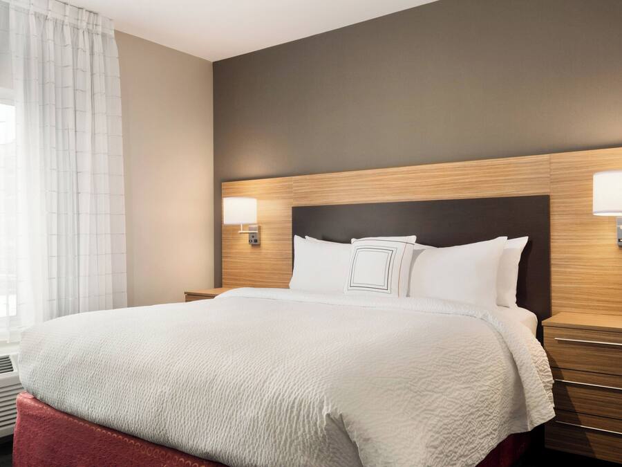 A hotel room with a large bed, wooden headboard, two bedside lamps, and a window with curtains.