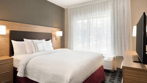 Ein Hotelzimmer mit einem großen Bett, einem Holzkopfteil, zwei Nachttischen mit Lampen, einem Flachbildfernseher und einem großen Fenster mit transparenten Vorhängen.