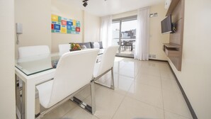 A modern living room with a glass dining table, white chairs, a sofa, a TV mounted on the wall, and a balcony with a view. - X52 Independencia Apartment (Córdoba)