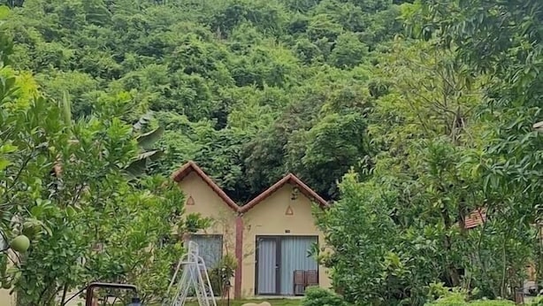 A person sitting on a stone pathway in a lush garden with a house in the background. - Trang An Retreat (Tay Hoa Lu)