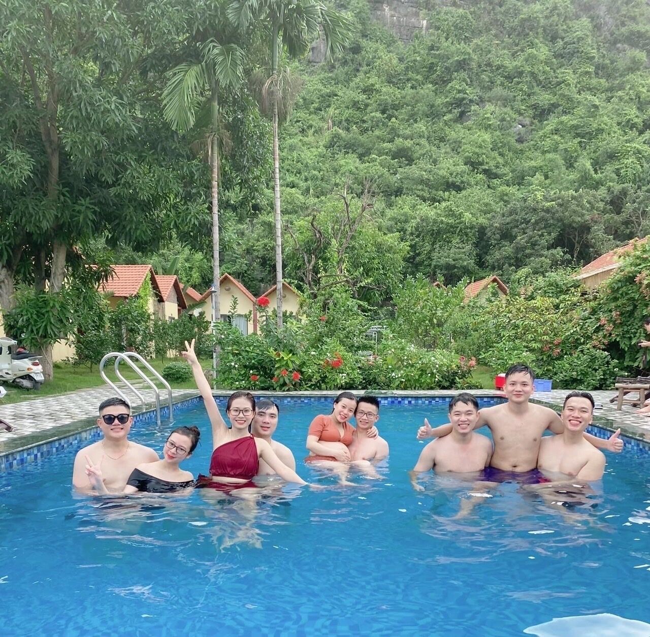 A group of people in a swimming pool surrounded by lush greenery and houses with red roofs.