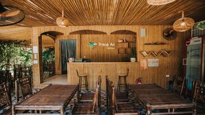 A restaurant with a bamboo interior, wooden tables and chairs, and a reception desk. - Trang An Retreat (Tay Hoa Lu)