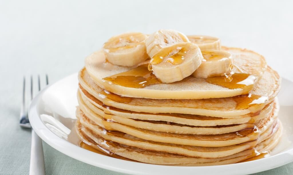 A stack of pancakes with banana slices and syrup on a white plate.