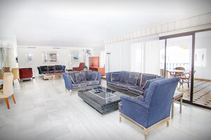 A spacious living room with a large sofa set, a coffee table, and a dining area with a table and chairs.