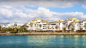 Un hotel costero con varios edificios blancos, un muro de piedra y una montaña al fondo.