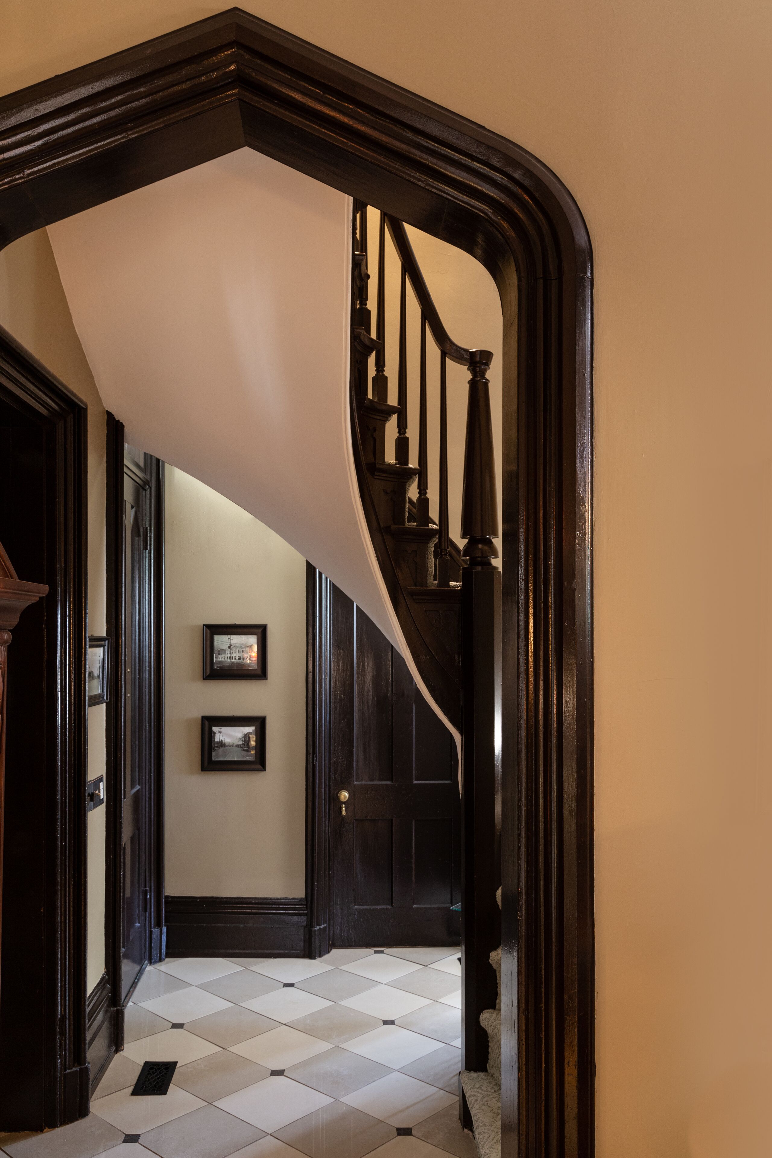 A hallway with a black and white checkered floor, a dark wooden staircase, and two framed pictures on the wall.