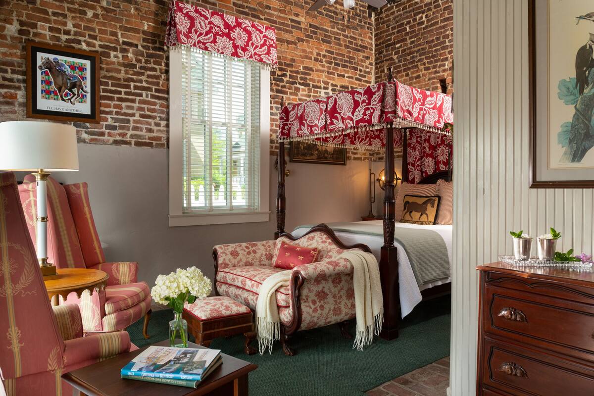 Une chambre à coucher avec un lit à baldaquin, un canapé aux motifs rouges et blancs, une table de chevet en bois et une moquette verte.