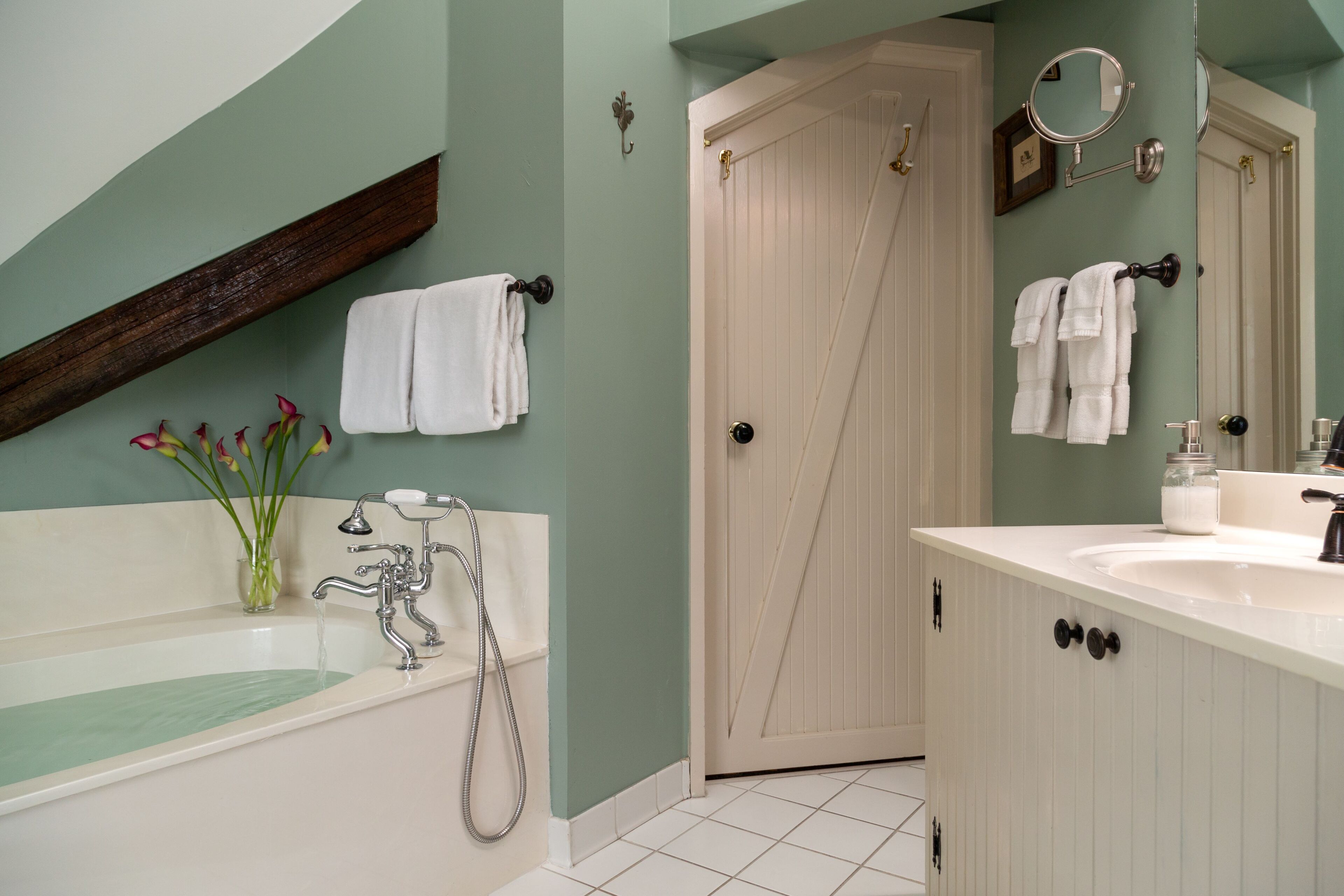 A bathroom with a bathtub, a shower, a sink, and a door.