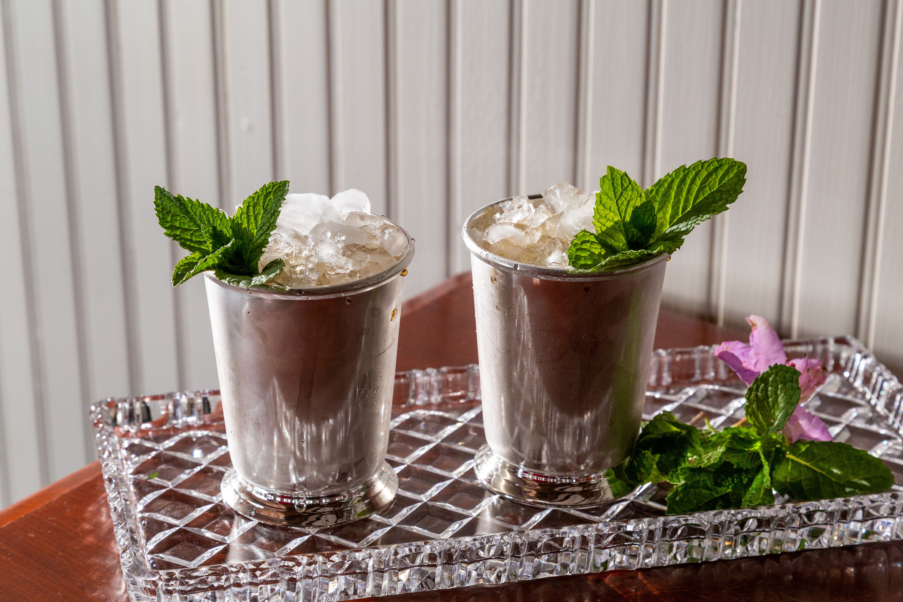 Deux verres de boisson glacée, décorés de feuilles de menthe, sont posés sur un plateau en verre.