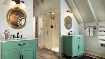 A bathroom with a white sink, a green vanity, a round mirror with a gold frame, and a glass shower enclosure.