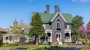 Una casa grande e histórica con techo verde, varias chimeneas y un porche delantero destacado.