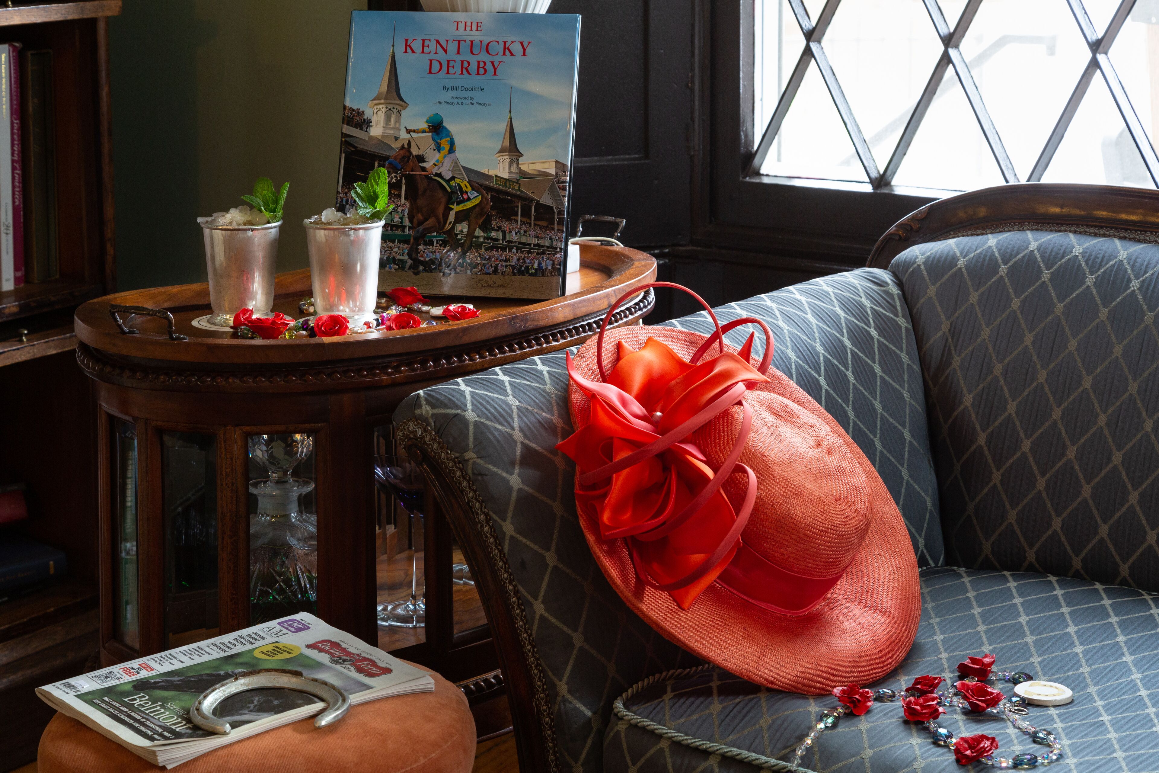Un libro con el título "The Kentucky Derby", un sombrero rojo y un collar decorativo con flores rojas.