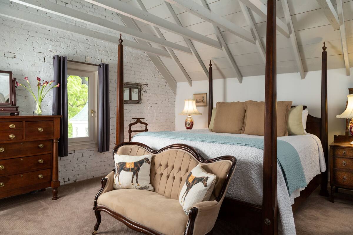 Une chambre à coucher avec un lit à baldaquin, une commode en bois et une chaise agrémentée de coussins à motifs équestres.