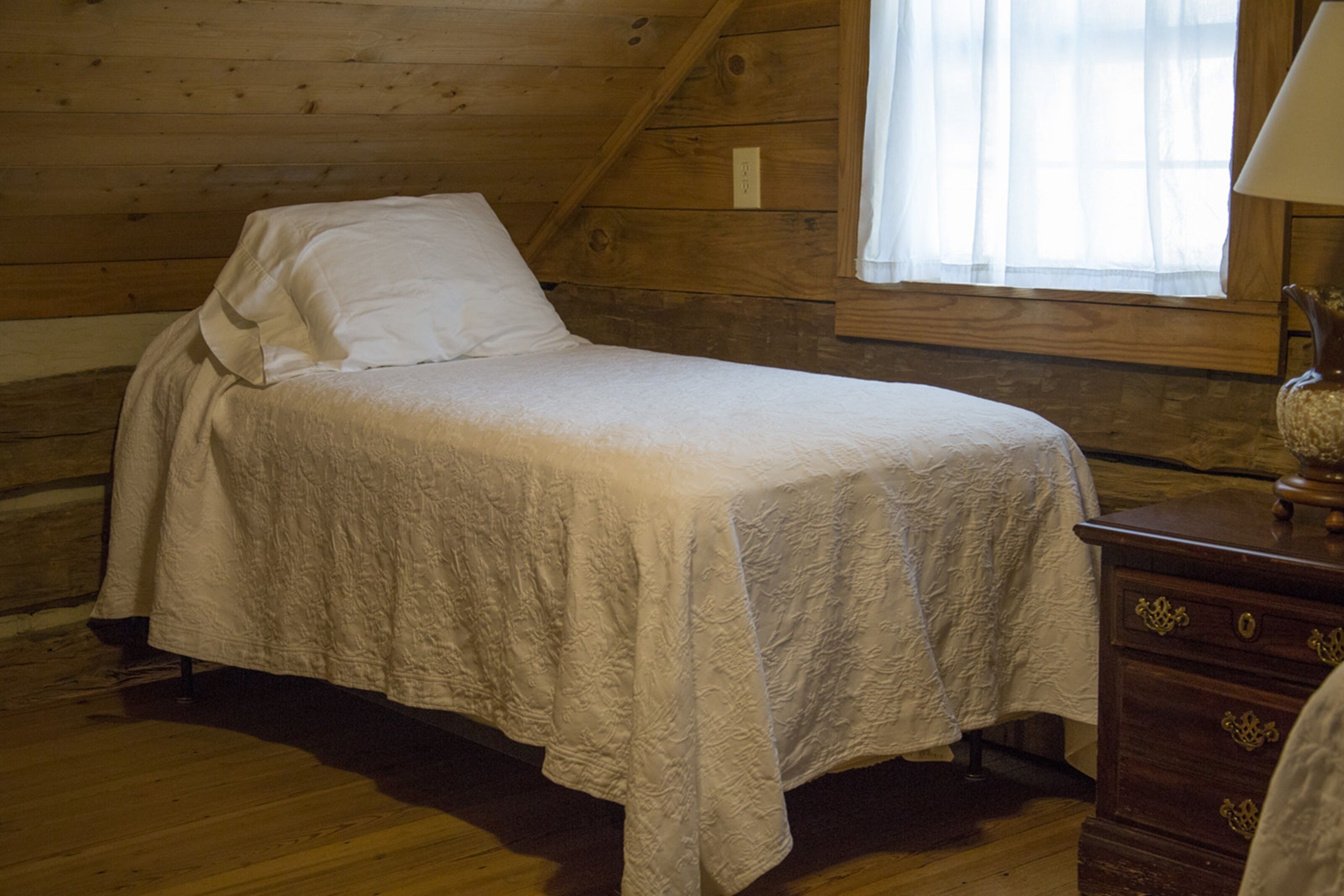 Un lit simple dans une chambre en bois, avec une fenêtre et une table de chevet.