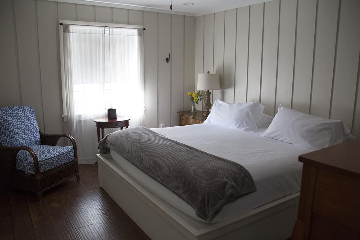 A hotel room with a large bed, a chair, a nightstand with a lamp, and a window with curtains.