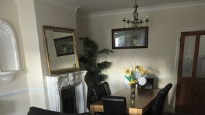 A living room with a brown leather sofa, a fireplace, a dining table with chairs, and a chandelier. - The Rhinos 2 (Enfield)