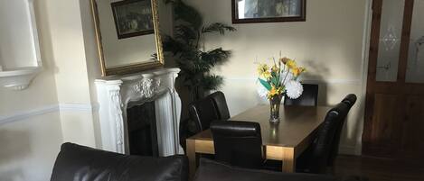 Una sala de estar con un sofá de cuero marrón, una chimenea, una mesa de comedor con sillas y una araña.