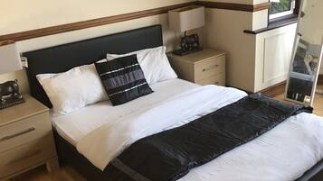 Una cama bien hecha con ropa de cama blanca y negra, un cabecero de madera y una mesita de noche con una lámpara y una figurita de un cerdo.