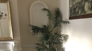A room with a wooden dining table, a black chair, a potted plant, a white fireplace, and a framed painting on the wall. - The Rhinos 2 (Enfield)