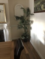 Una habitación con una mesa de comedor de madera, una silla negra, una planta en maceta, una chimenea blanca y un cuadro en la pared.