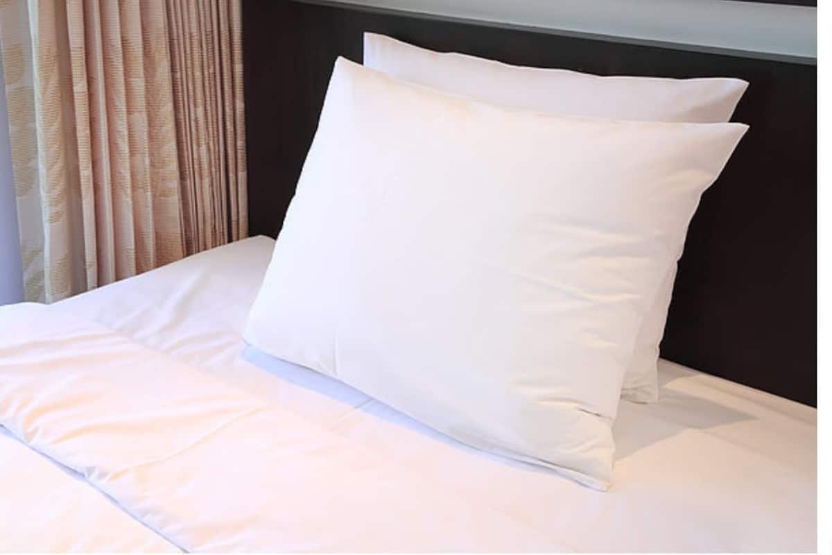 A neatly made bed with white bedding and pillows, a dark headboard, and a window with curtains.
