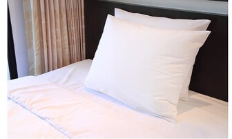 Una cama bien hecha con ropa blanca y almohadas, un cabecero oscuro y una cortina con estampado de hojas.