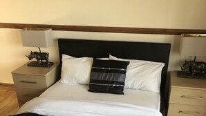 Cama bem arrumada com roupa de cama branca e preta, cabeceira e mesas de cabeceira com abajures e objetos decorativos.
