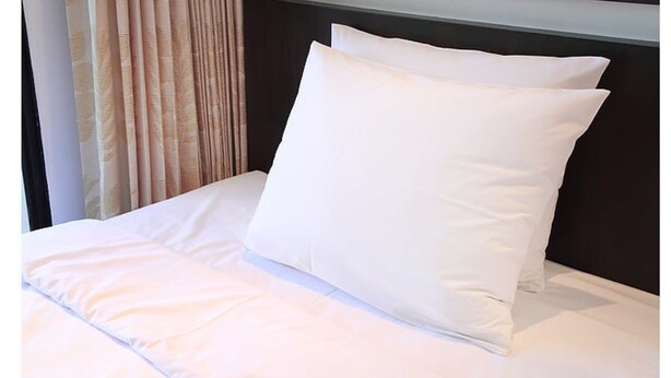 Uma cama bem arrumada com roupa de cama e almofadas brancas, uma cabeceira escura e um cortinado com padrão de folhas.