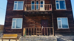Ein zweistöckiges Holzhaus mit Balkon, Eingangstür und Bank vor der Fassade.