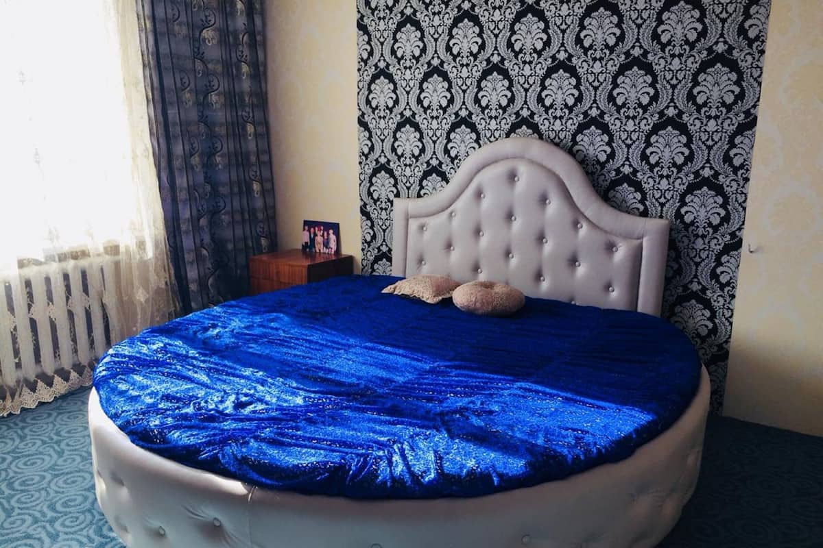 Ein rundes Bett mit einer gepolsterten Kopfteil, einer blauen Satins Bettdecke und zwei Kissen.
