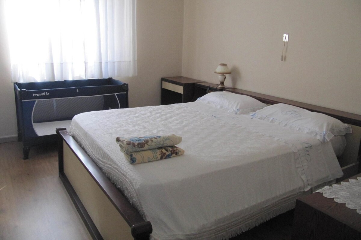 A bedroom with a bed, a bedside table, a lamp, and a window with curtains.